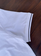 Side view of white polo shirt hem with black-trim sleeve edge detail.