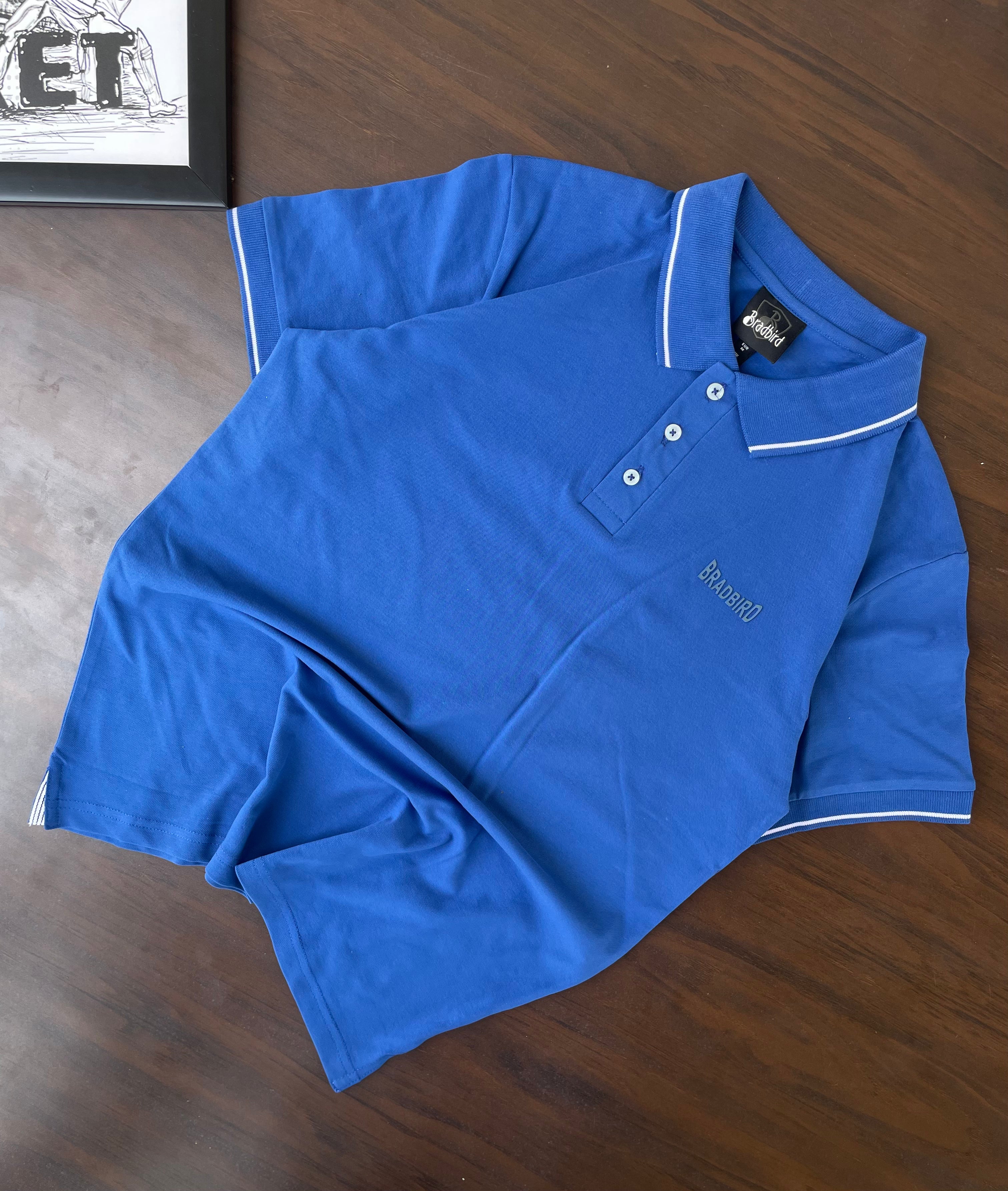 Blue polo shirt folded with white tipping trim and Bradbird chest logo