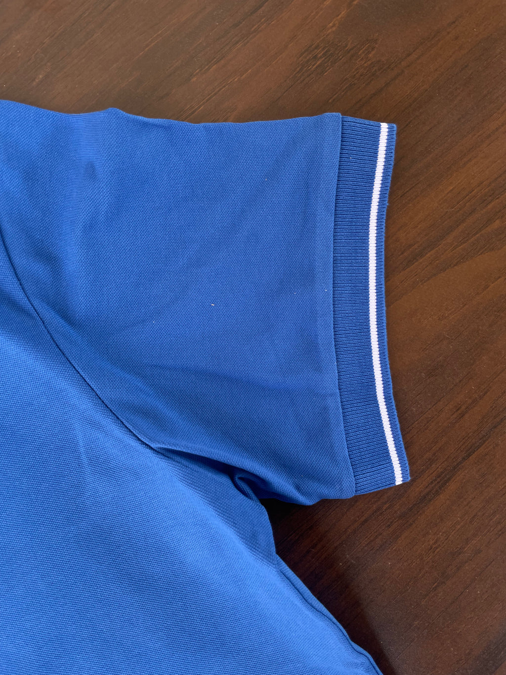 Blue polo shirt sleeve with white tipping stripe on ribbed hem