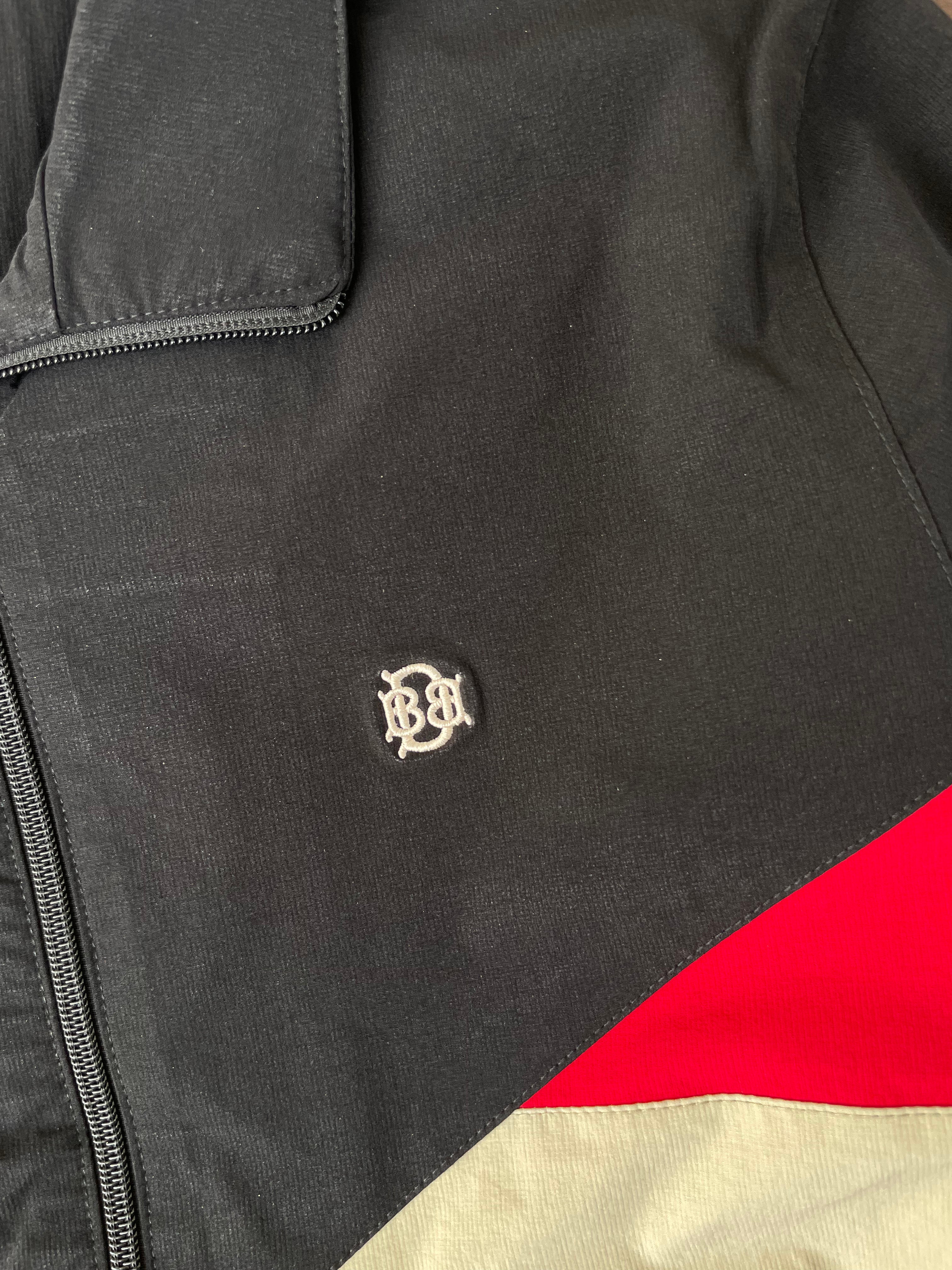 Black windbreaker with small chest logo and red color-block panel; visible zipper edge