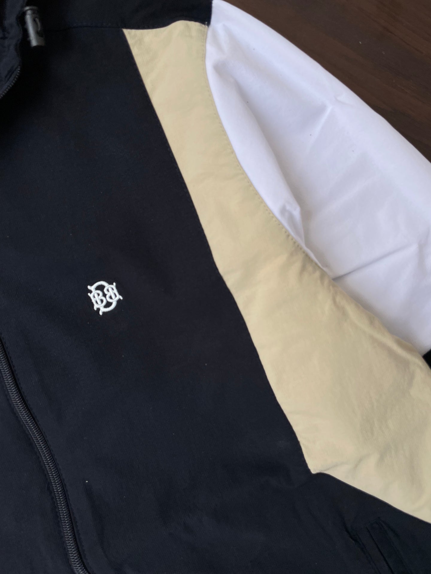 Black windbreaker chest logo with sand and white diagonal panel detail
