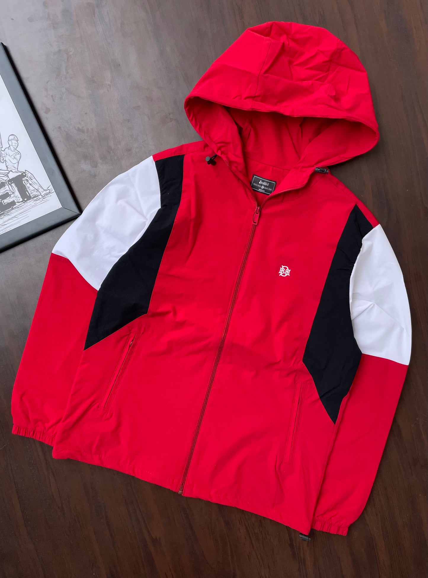 Scarlet red hooded windbreaker jacket with black and white sleeve panels, laid flat