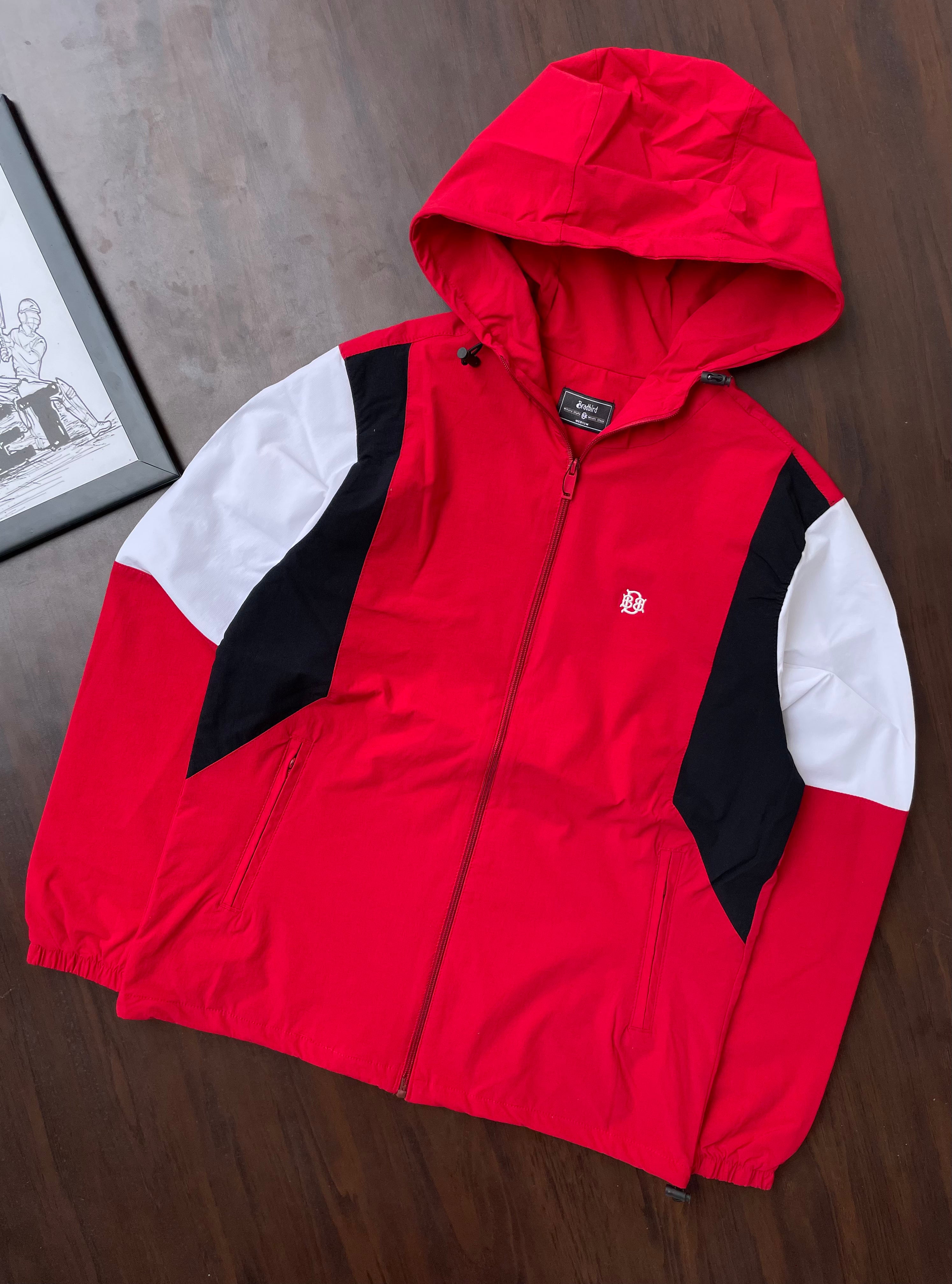 Scarlet red hooded windbreaker jacket with black and white sleeve panels, laid flat