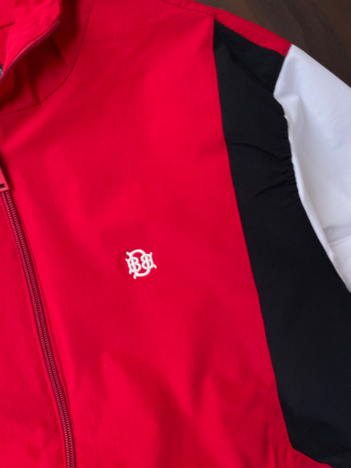 Scarlet red jacket front with zipper and small white logo, black side panel