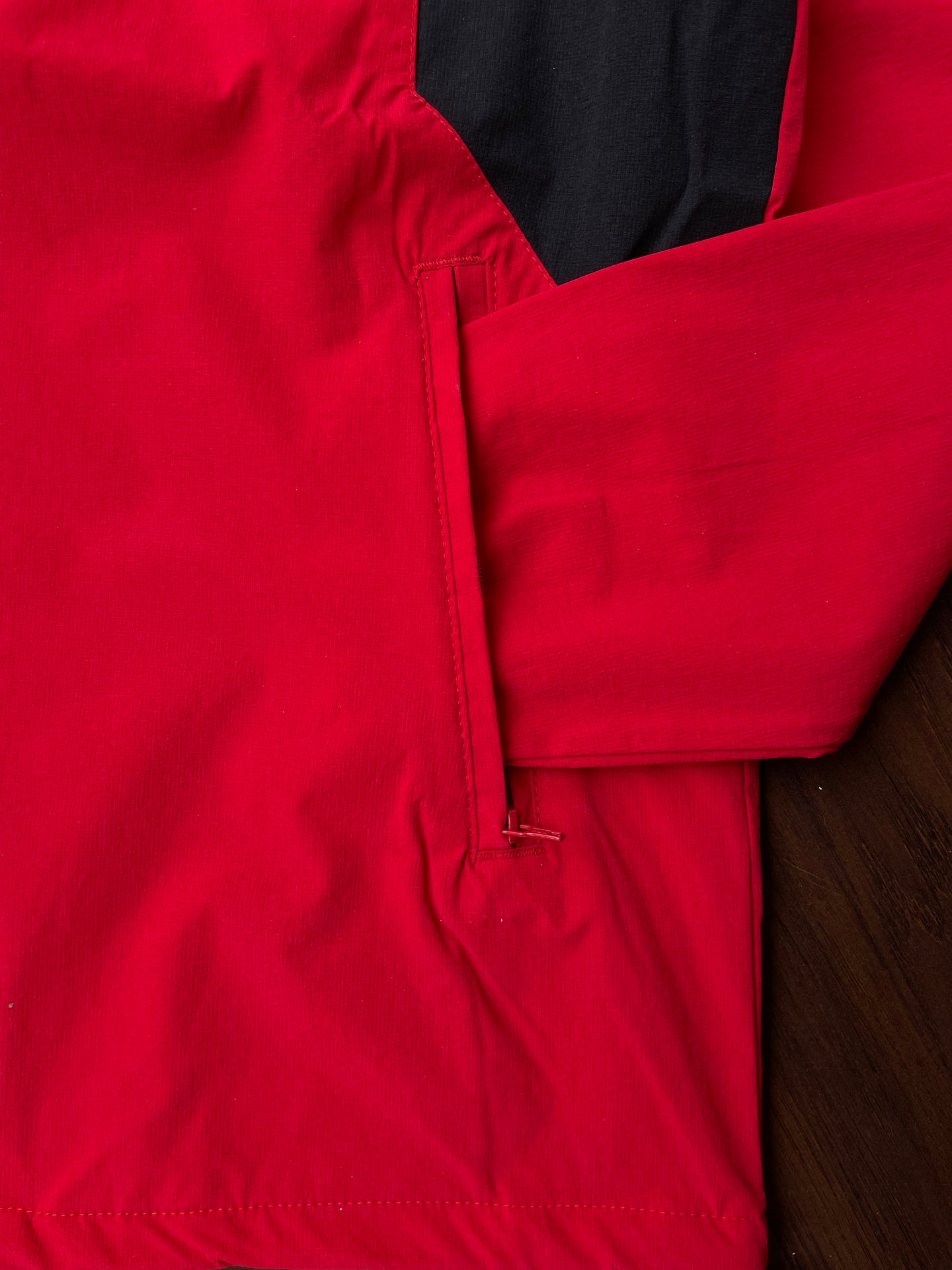 Scarlet red windbreaker cuff and pocket seam, black interior panel visible