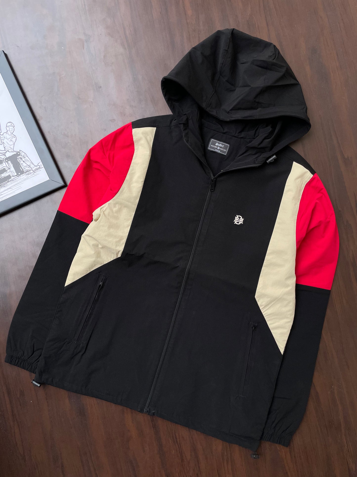 Black hooded windbreaker jacket with red sleeves and sand center panels, full zipper