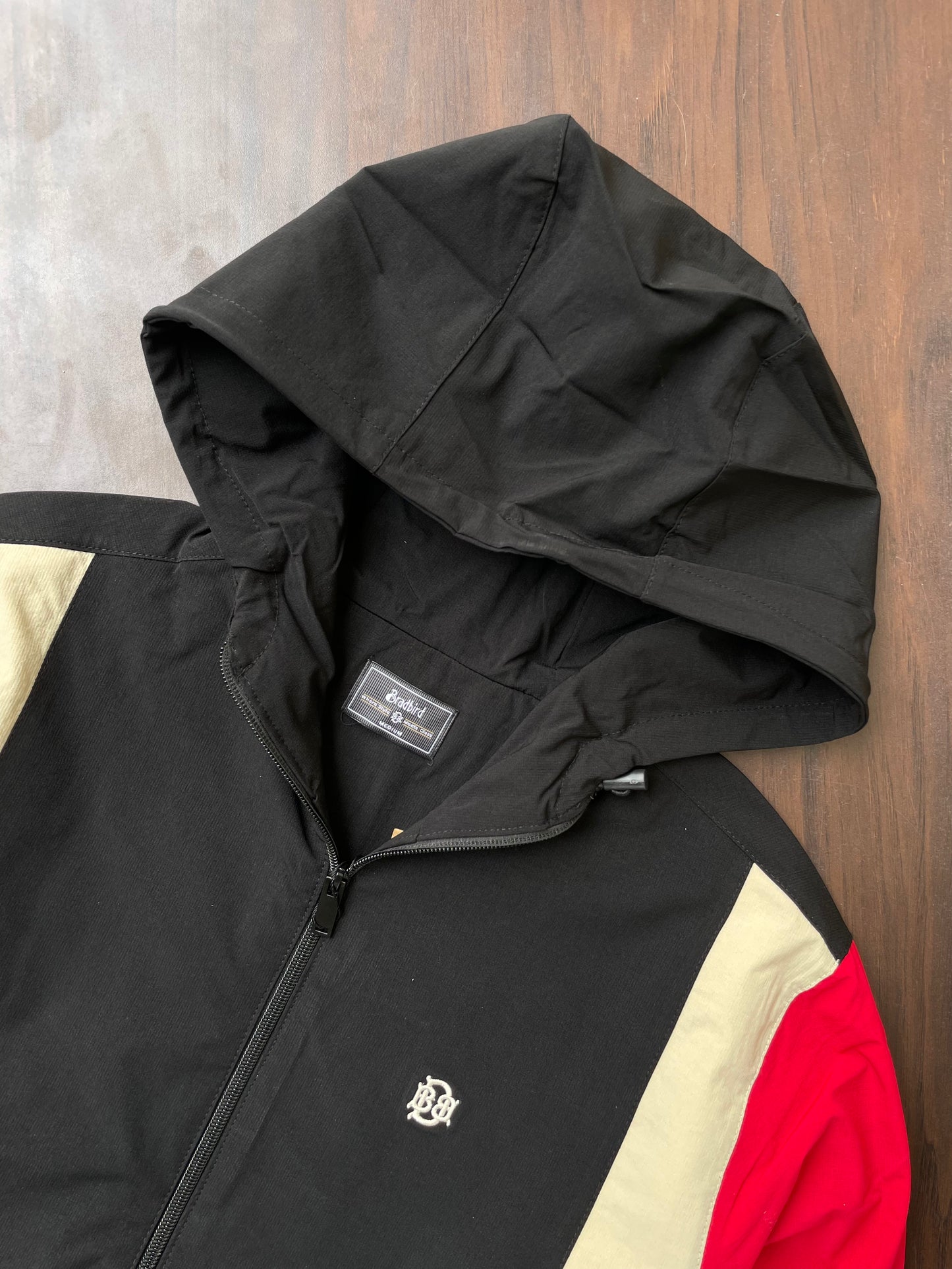Black hooded windbreaker close-up with front zipper; sand and red accent panel