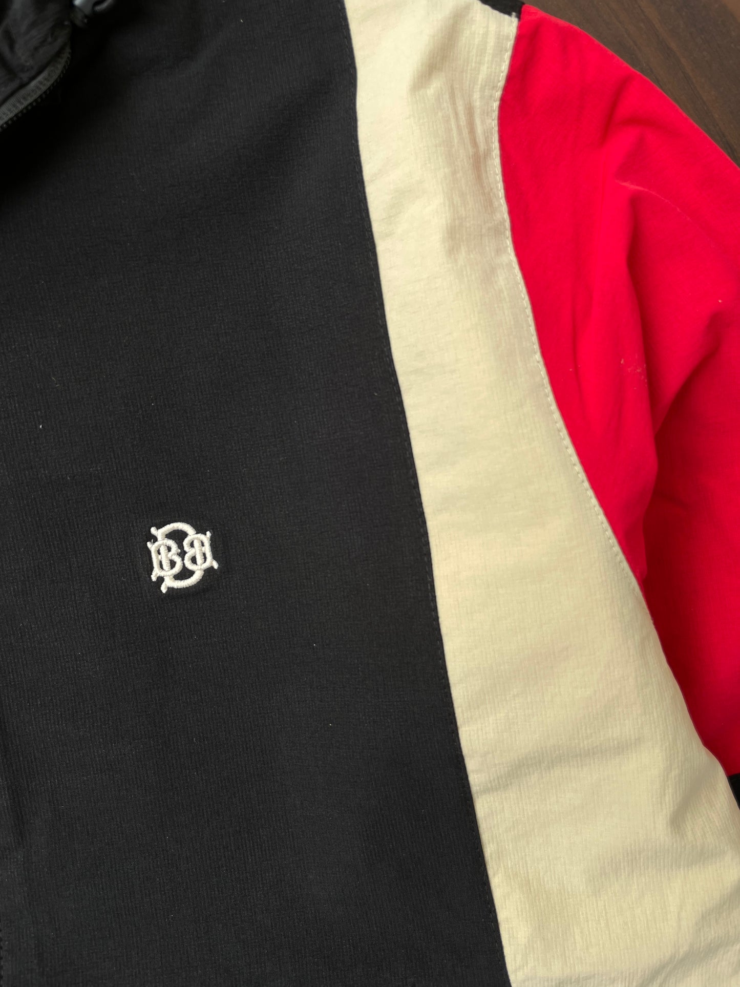 Black windbreaker chest logo with sand-and-red curved stripe panel