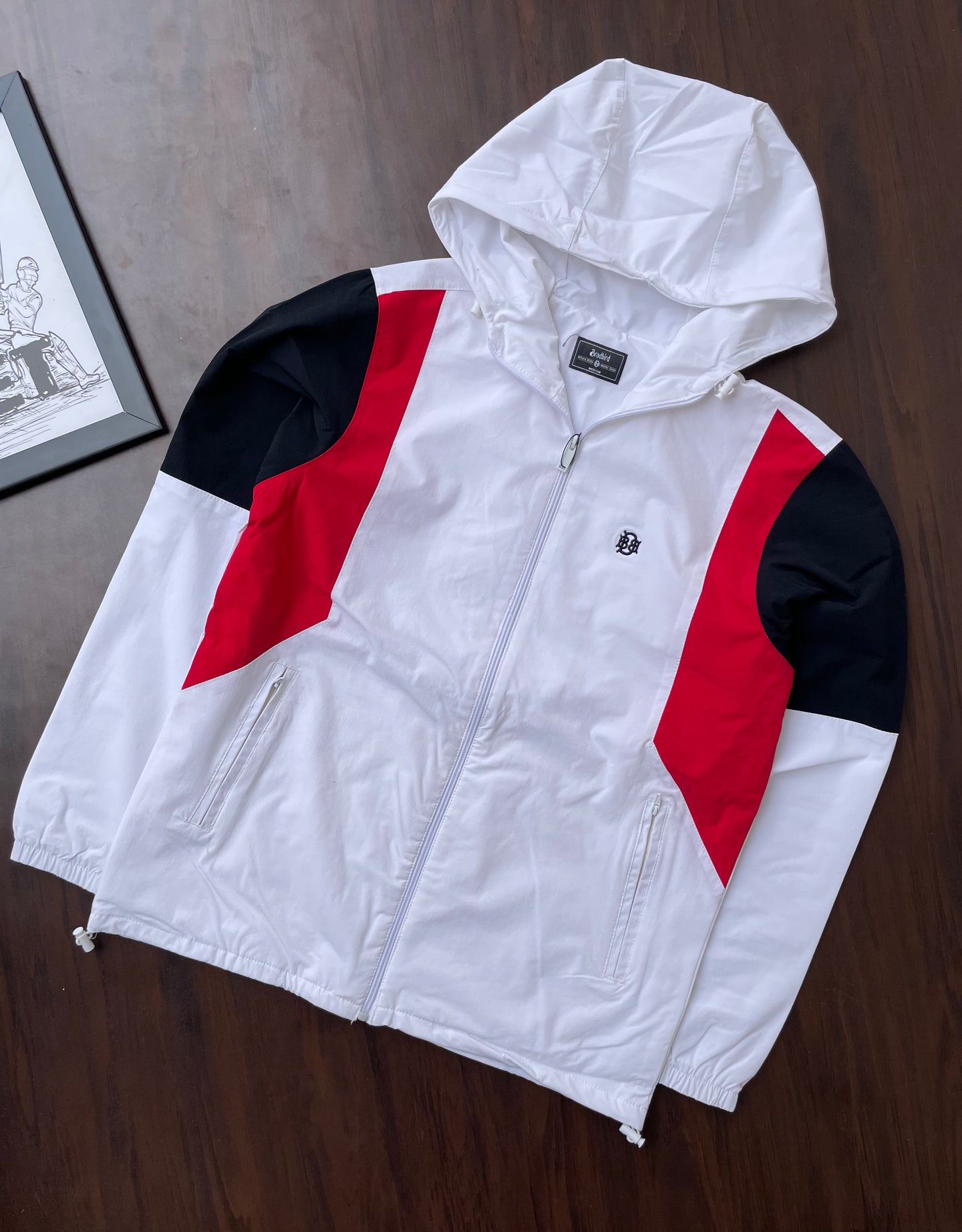 White hooded windbreaker with red and black chevron panels, zip front, standing collar