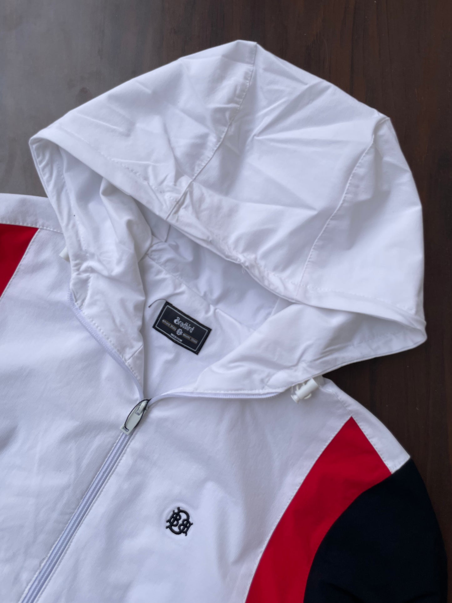 White hooded windbreaker close-up: hood and shoulder panel, zip pull, logo