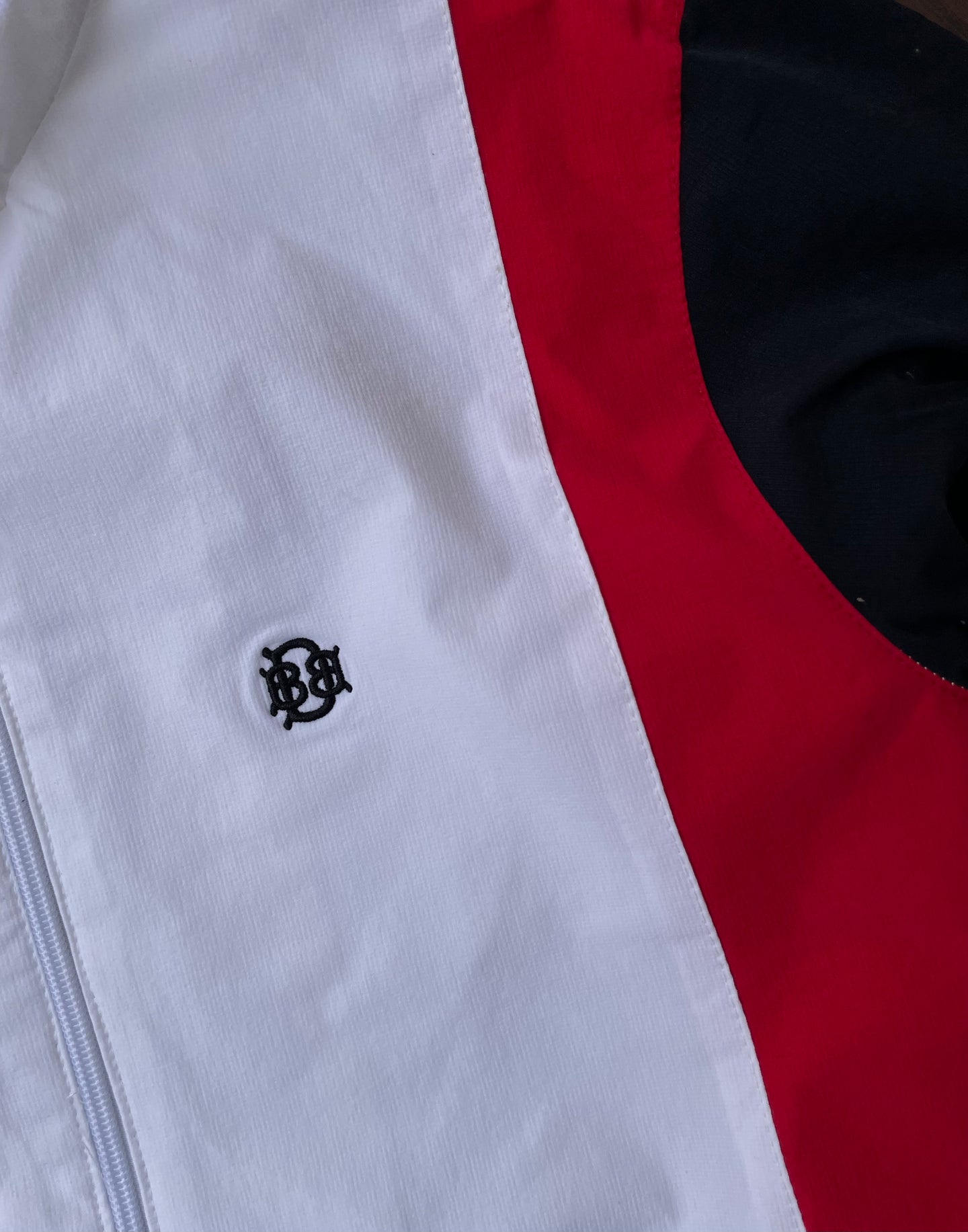 White windbreaker chest logo with red and black curved panel detail