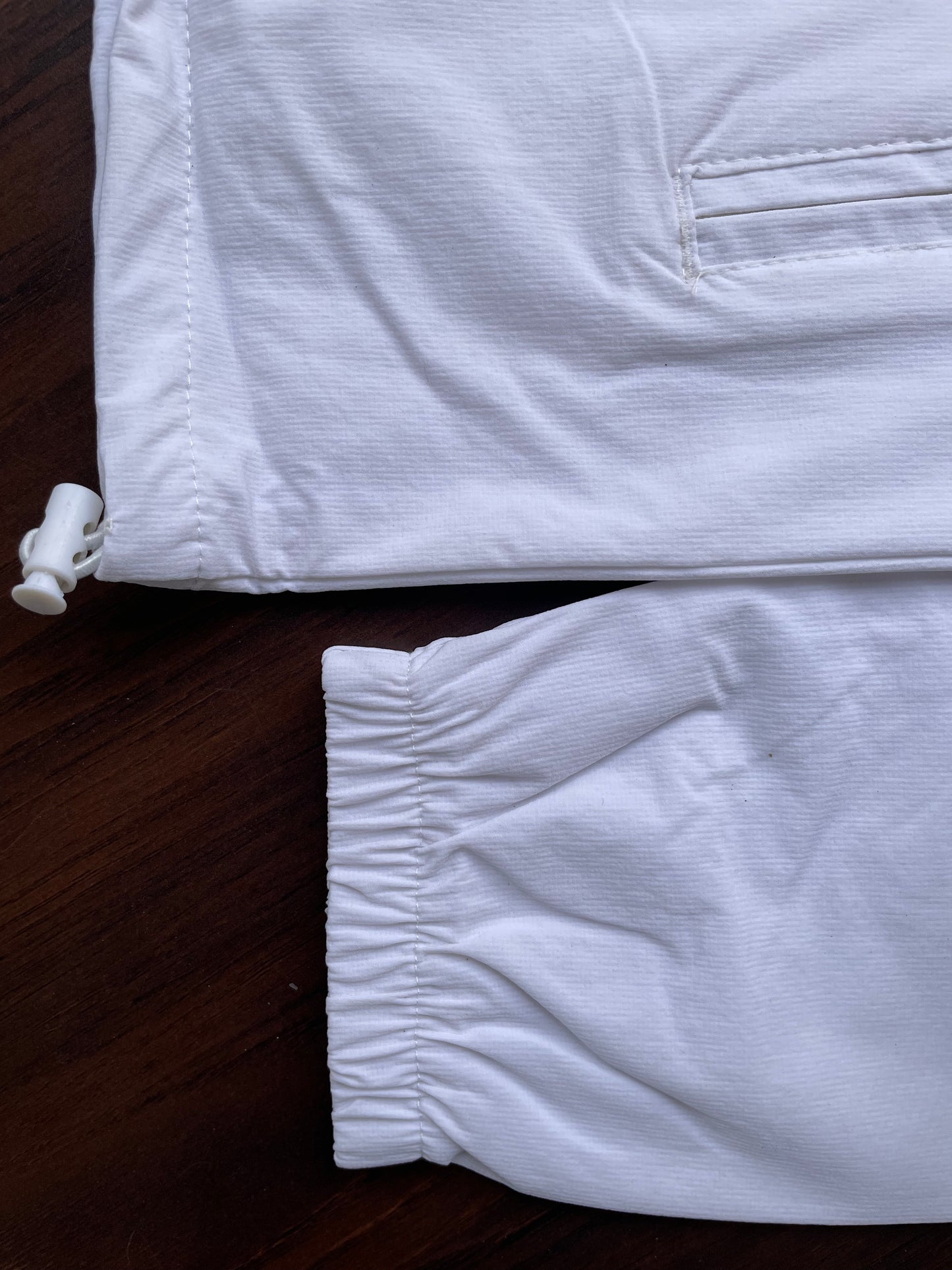 White windbreaker hem with elastic cuff and side pocket opening, drawcord ends visible