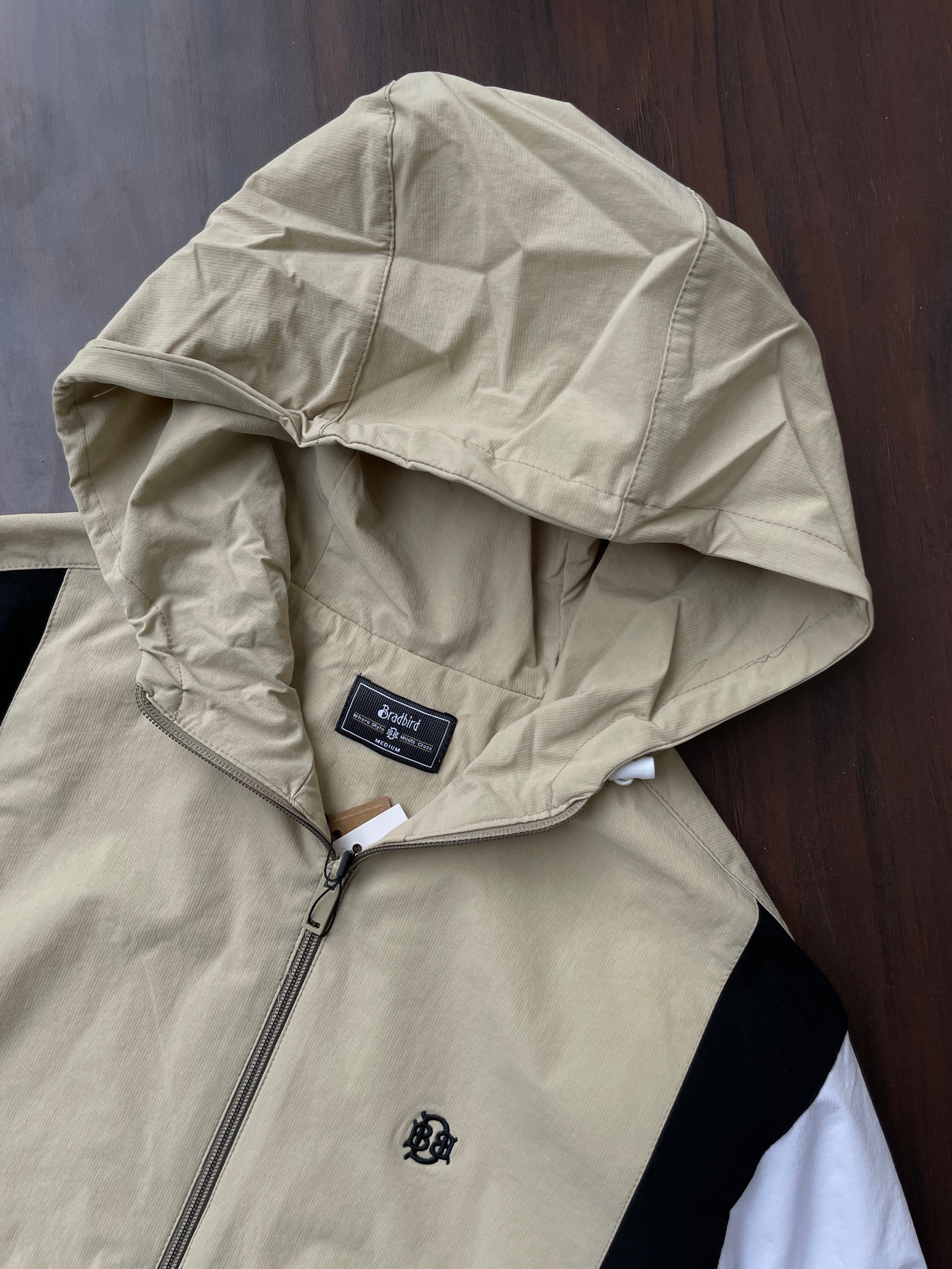 Beige hooded windbreaker close-up with adjustable hood, front zip, chest logo