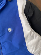 Blue windbreaker chest logo with white-and-black diagonal sleeve panel