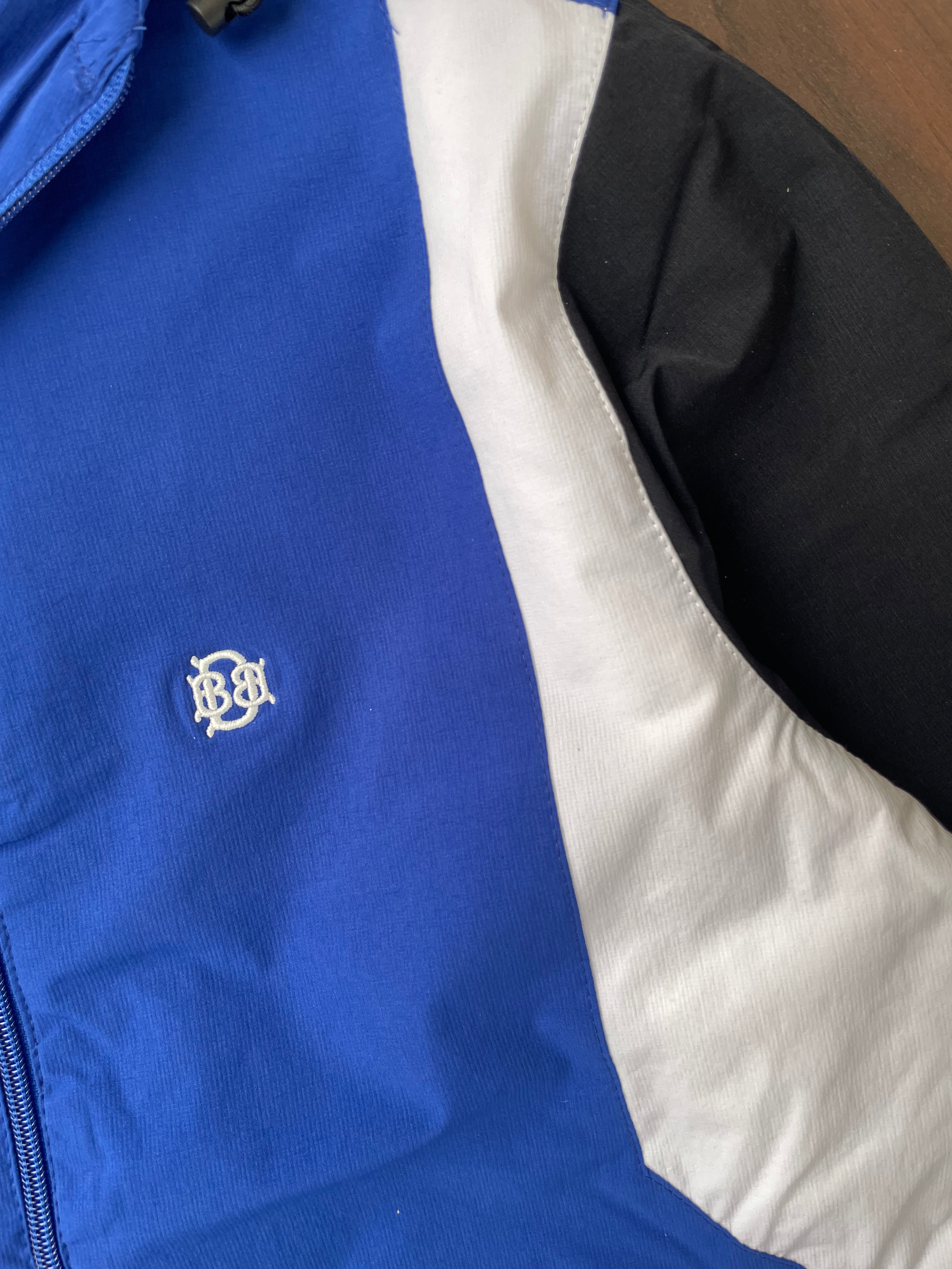 Blue windbreaker chest logo with white-and-black diagonal sleeve panel