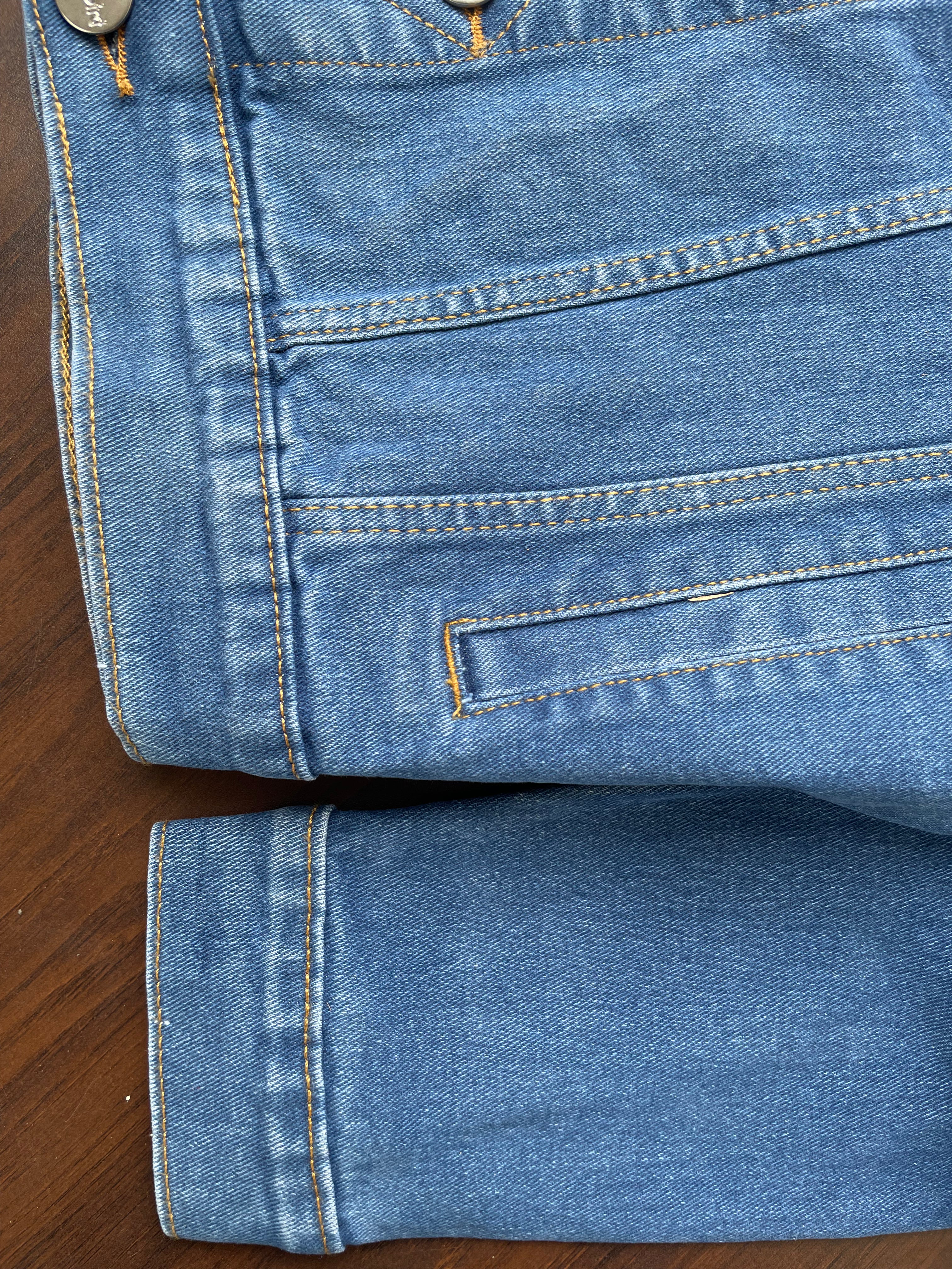 Bottom hem and sleeves of medium-wash denim jacket with topstitching