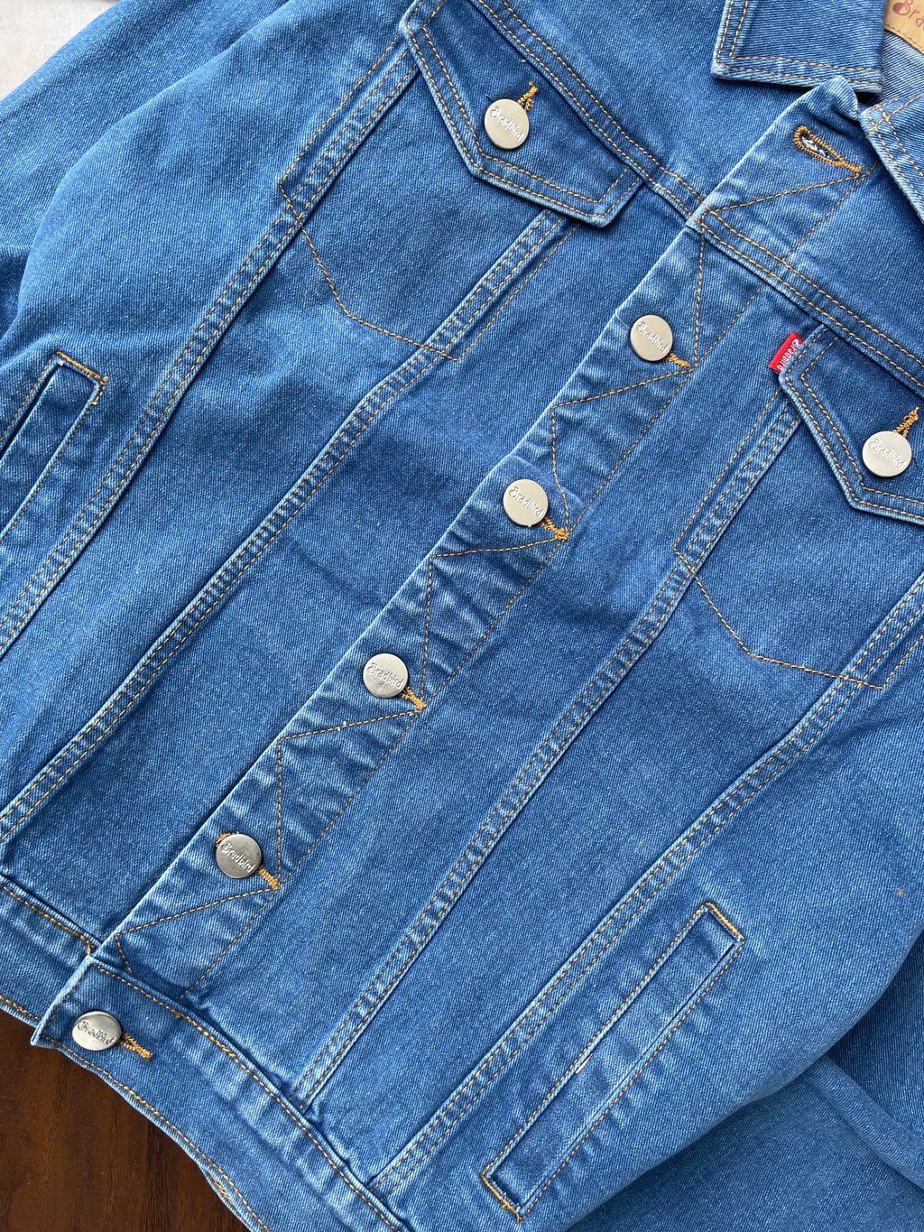 Medium-wash denim jacket back panel with seam lines and button snaps