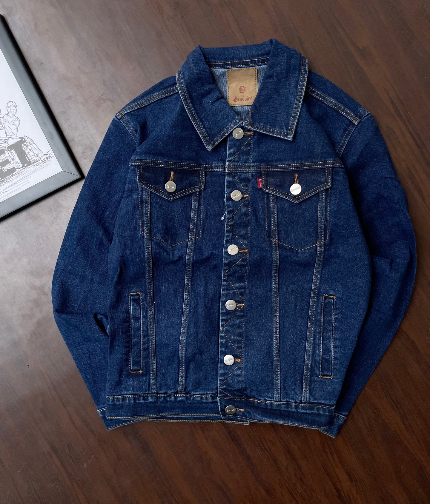 Men's dark blue denim jacket laid flat with button front and chest flap pockets