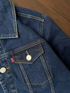 Denim jacket chest pocket detail with metal snap, yellow stitching, and brand patch