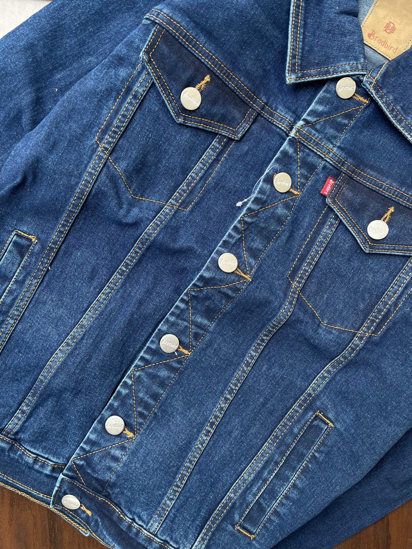 Dark-wash denim jacket back yoke and pockets close-up with buttons and seams