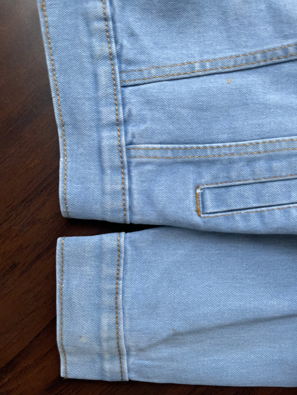 Light-wash denim jacket hem and cuff detail with buttoned placket and stitched edge.