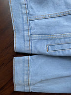 Light-wash denim jacket hem and cuff detail with buttoned placket and stitched edge.