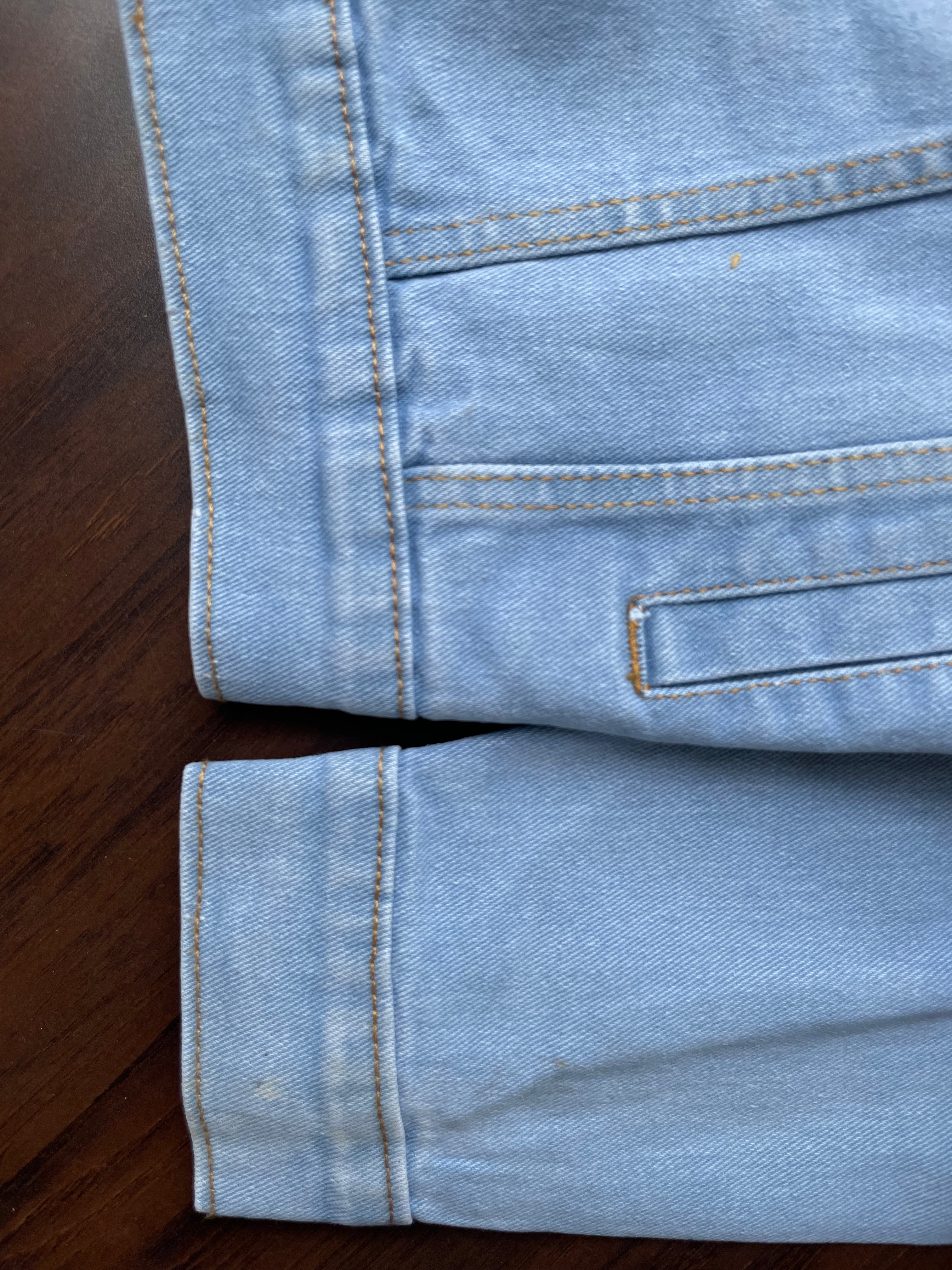 Light-wash denim jacket hem and cuff detail with buttoned placket and stitched edge.