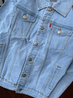 Light-wash denim jacket chest and waist pockets with metal buttons and stitch detailing.
