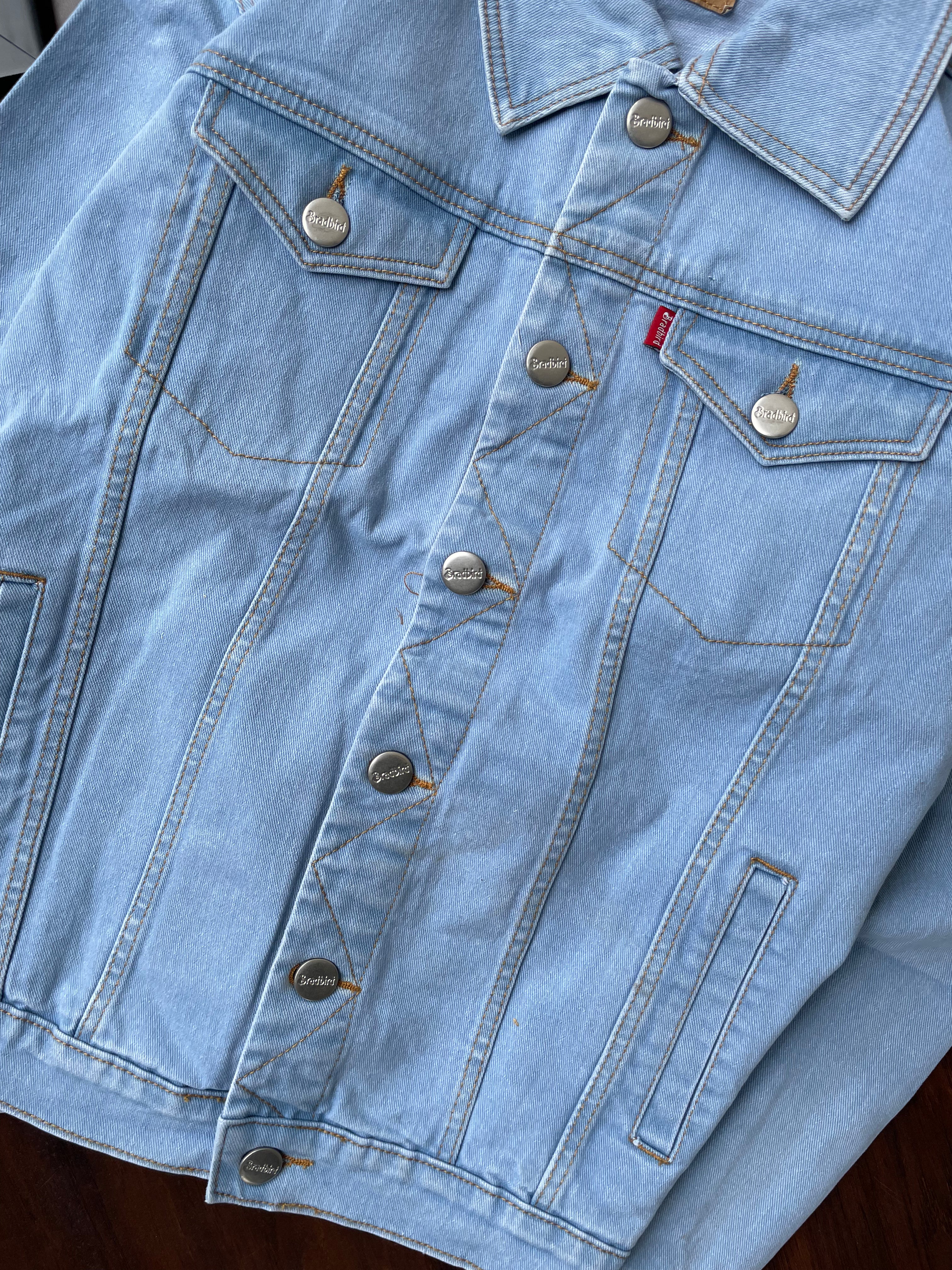 Light-wash denim jacket chest and waist pockets with metal buttons and stitch detailing.