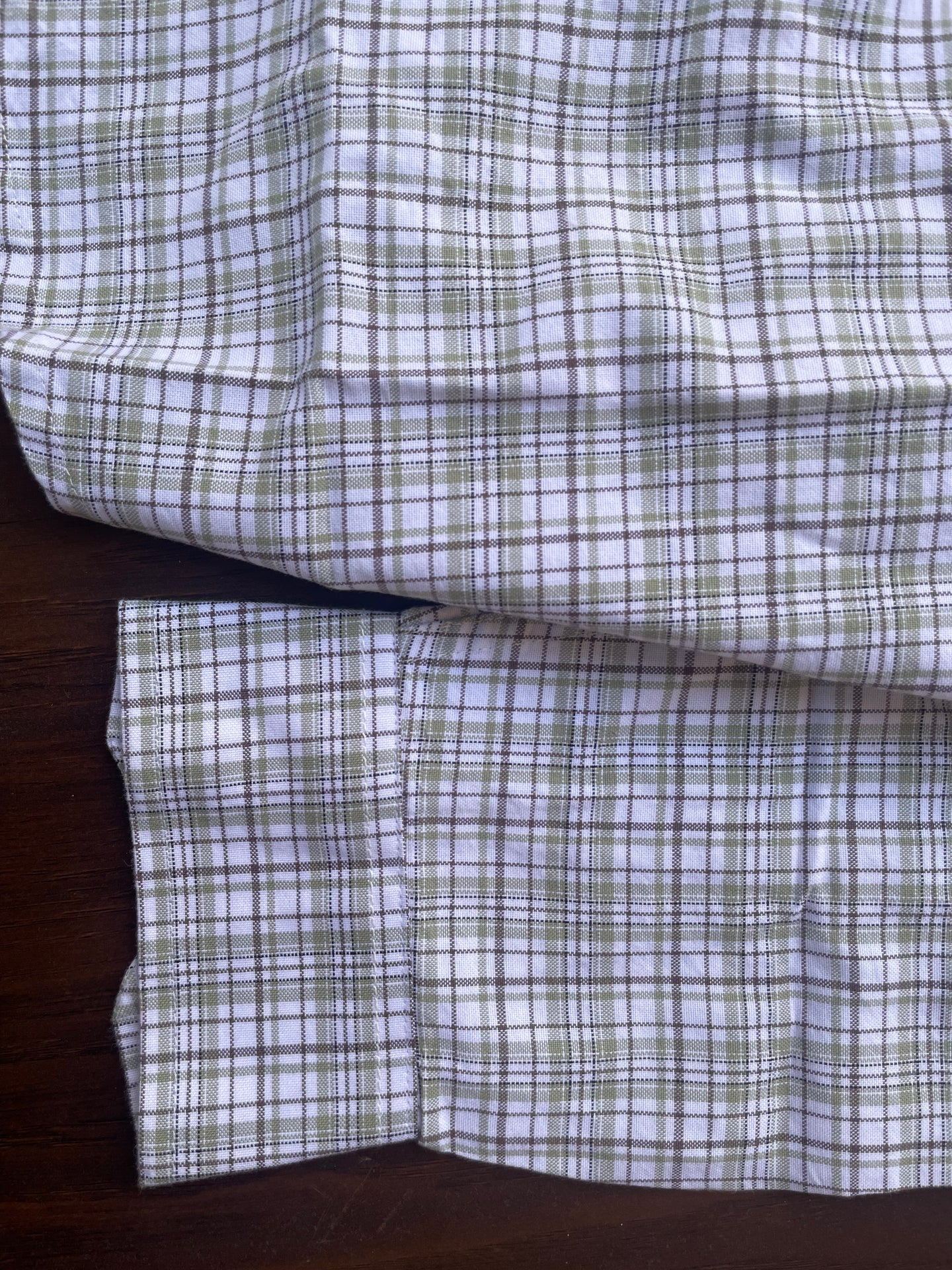 Sleeve and hem detail of plaid shirt, white with blue-grey and green grid checks