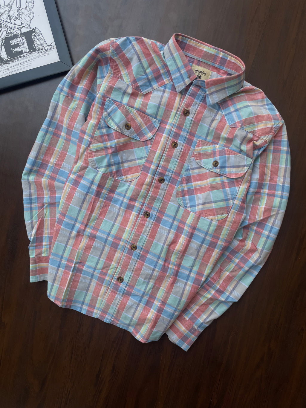 Folded casual shirt with bold red, blue, and green plaid; button front and chest pockets