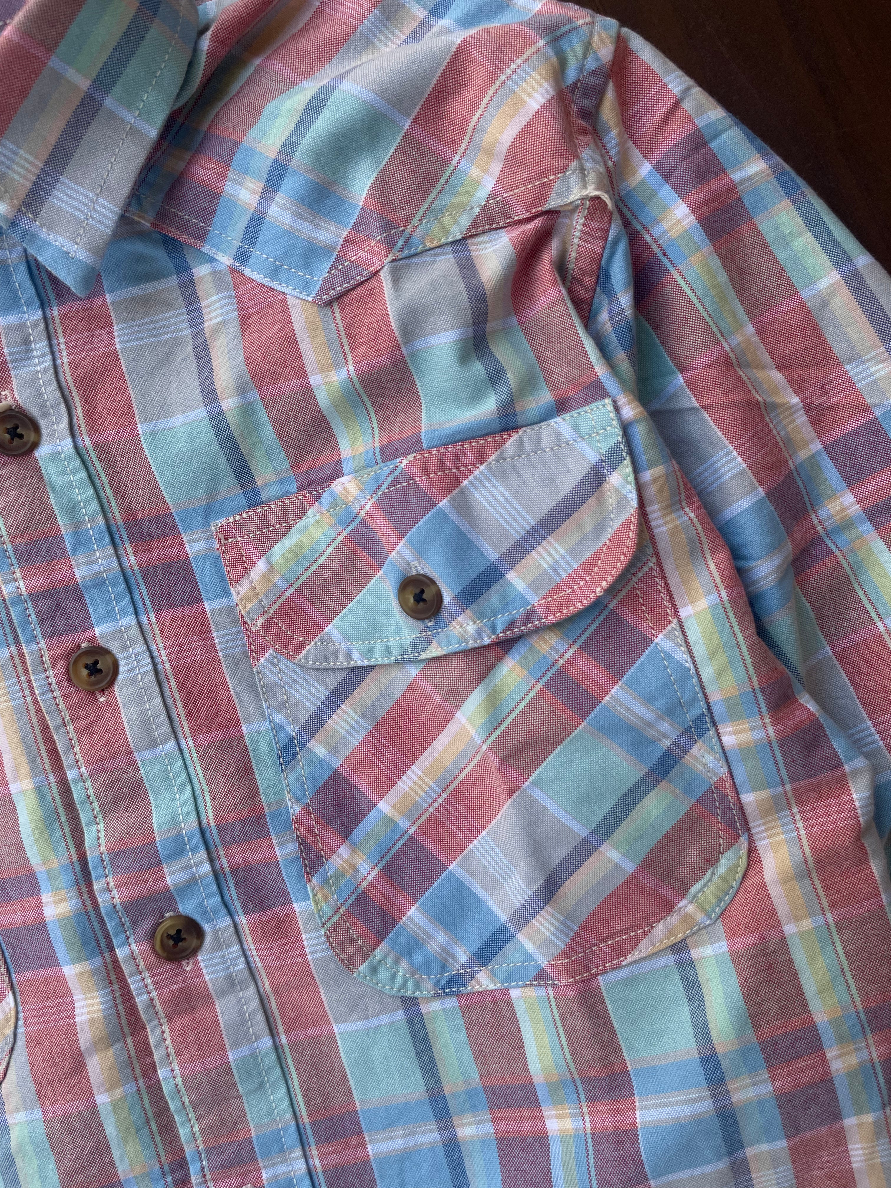 Red, blue, and green plaid shirt detail: chest pocket flap and brown buttons