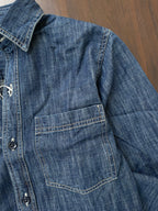 Mid-wash denim shirt close-up of chest pocket and button placket.