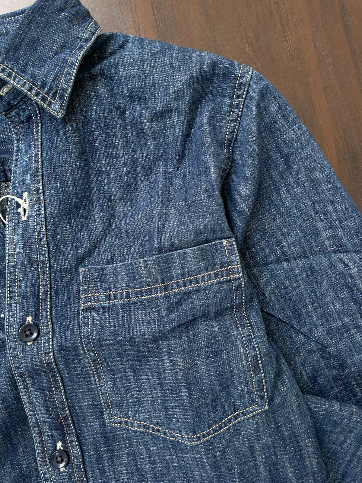 Mid-wash denim shirt close-up of chest pocket and button placket.