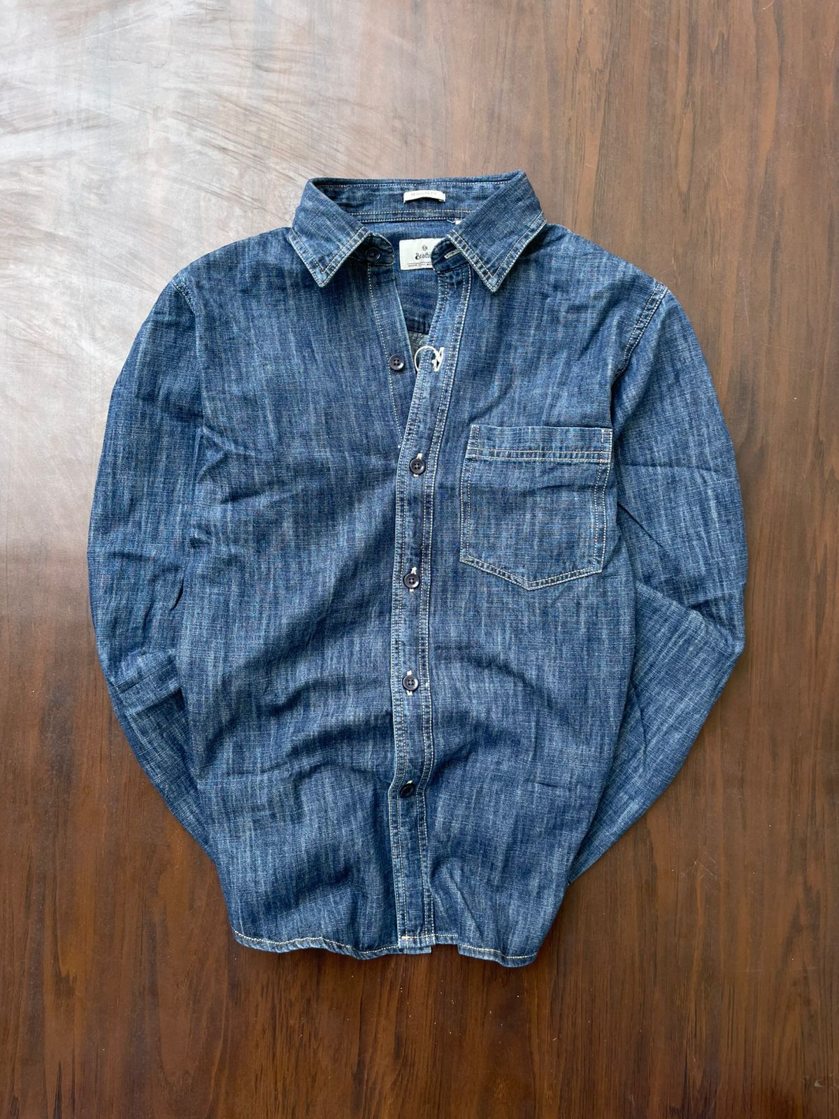Mid-wash denim shirt laid flat, button front and single chest pocket.
