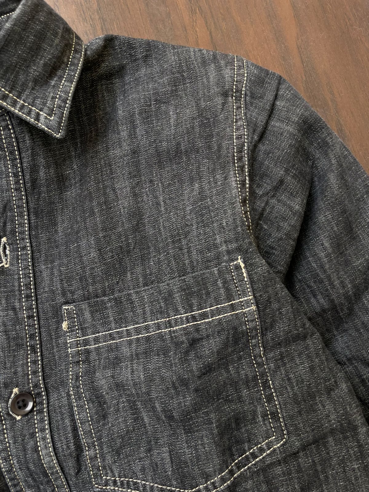 Deep grey denim shirt close-up of chest pocket with contrast stitching and button placket