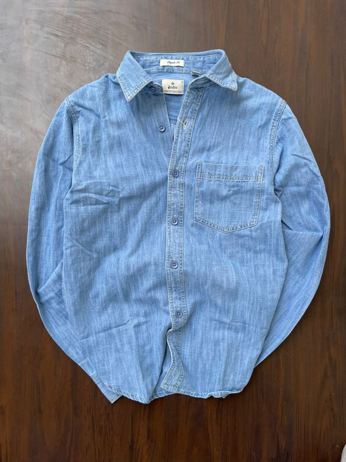 Light-wash denim button-up shirt on hanger, pointed collar, chest pocket, tonal buttons