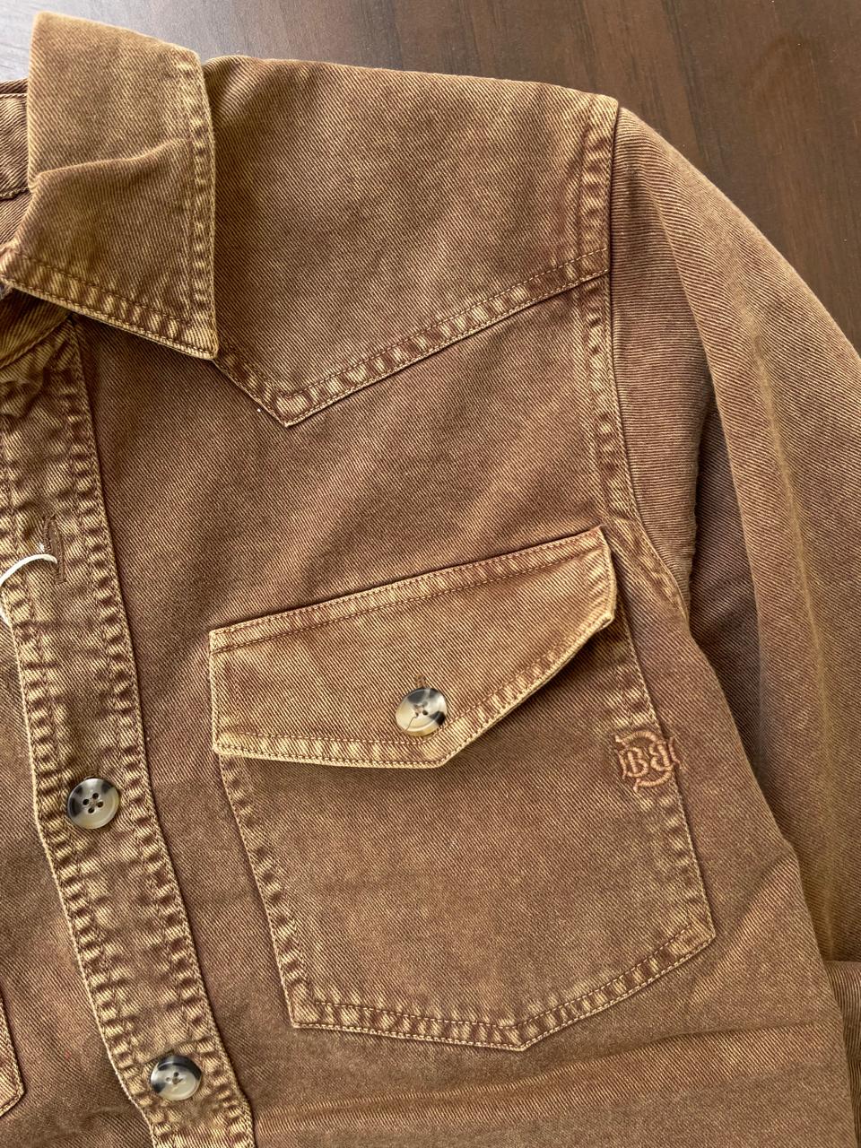 Brown denim chest pocket with metal snap button and contrast topstitching.