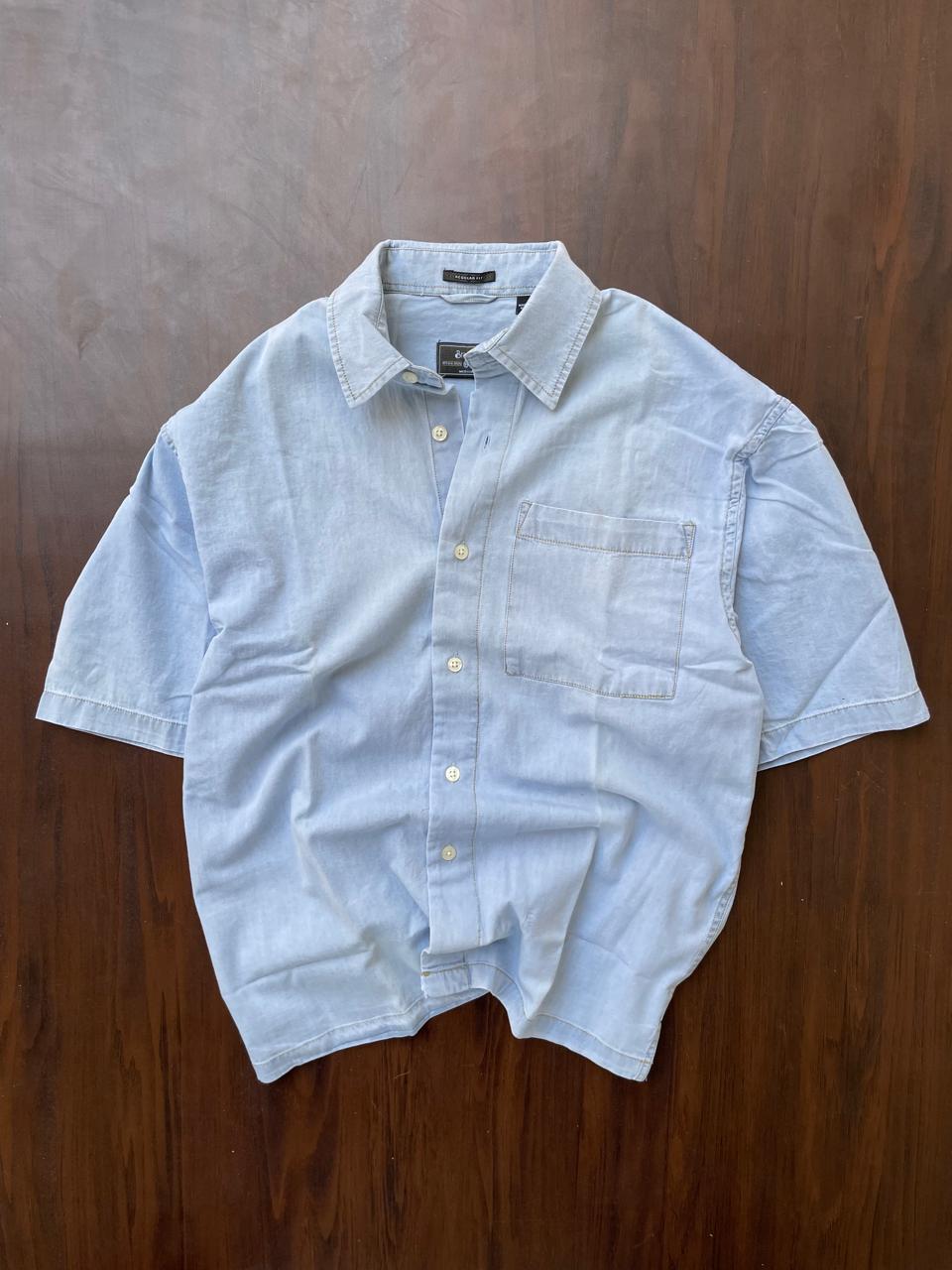 Powder blue denim half-sleeve shirt laid flat, button front and chest pocket