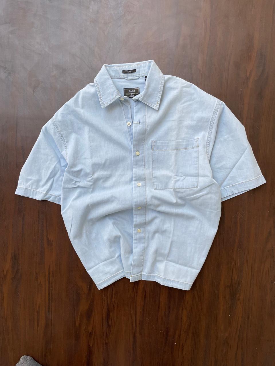 Light blue half-sleeve denim shirt folded flat, button placket and chest pocket