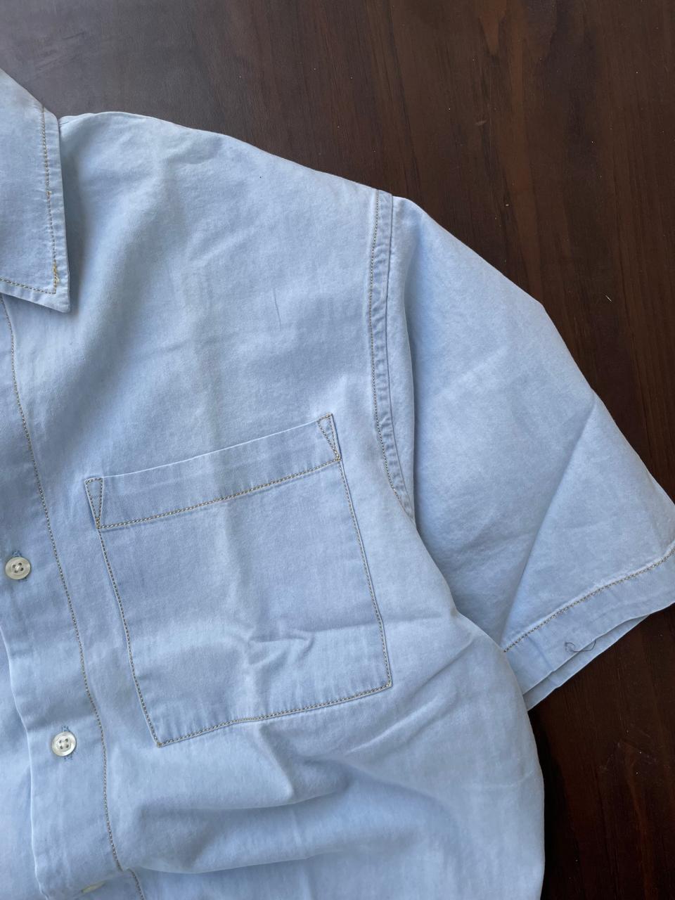 Light blue denim shirt sleeve and chest pocket close-up with contrast stitching