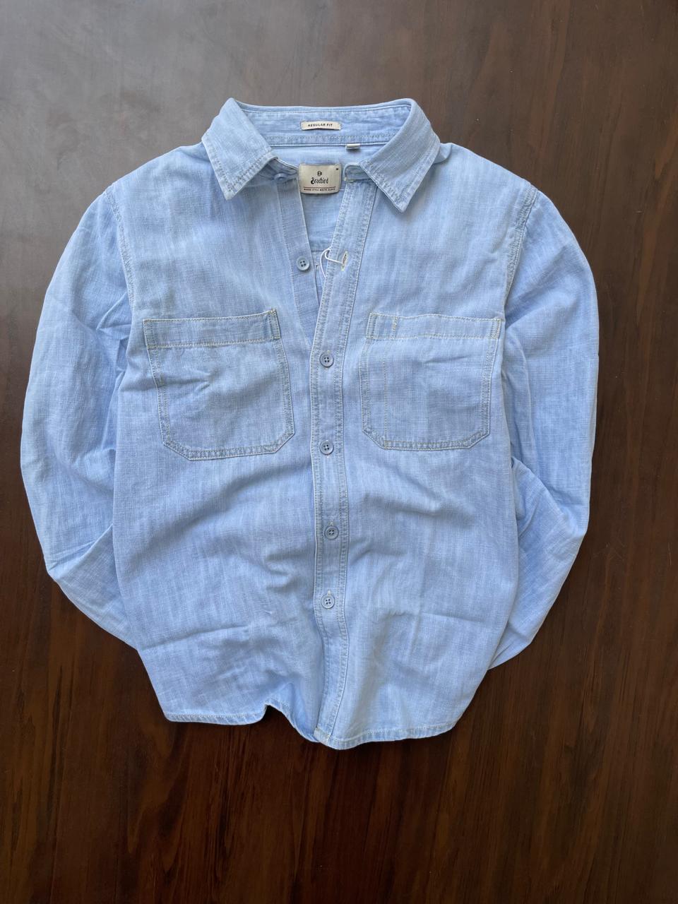 Men's light-wash denim shirt laid flat with point collar and two chest pockets