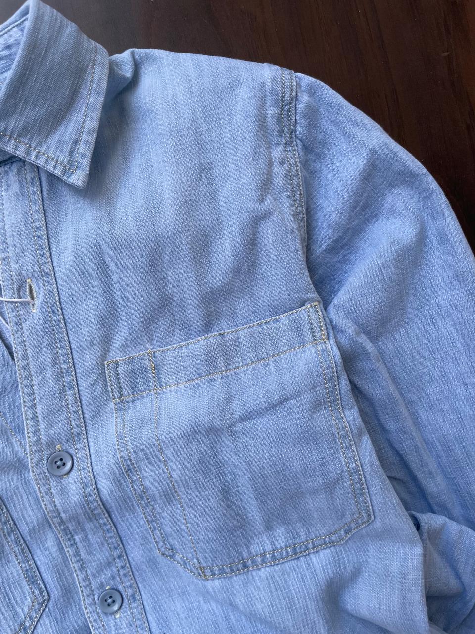 Men's light-wash denim shirt close-up of chest pocket and buttoned placket