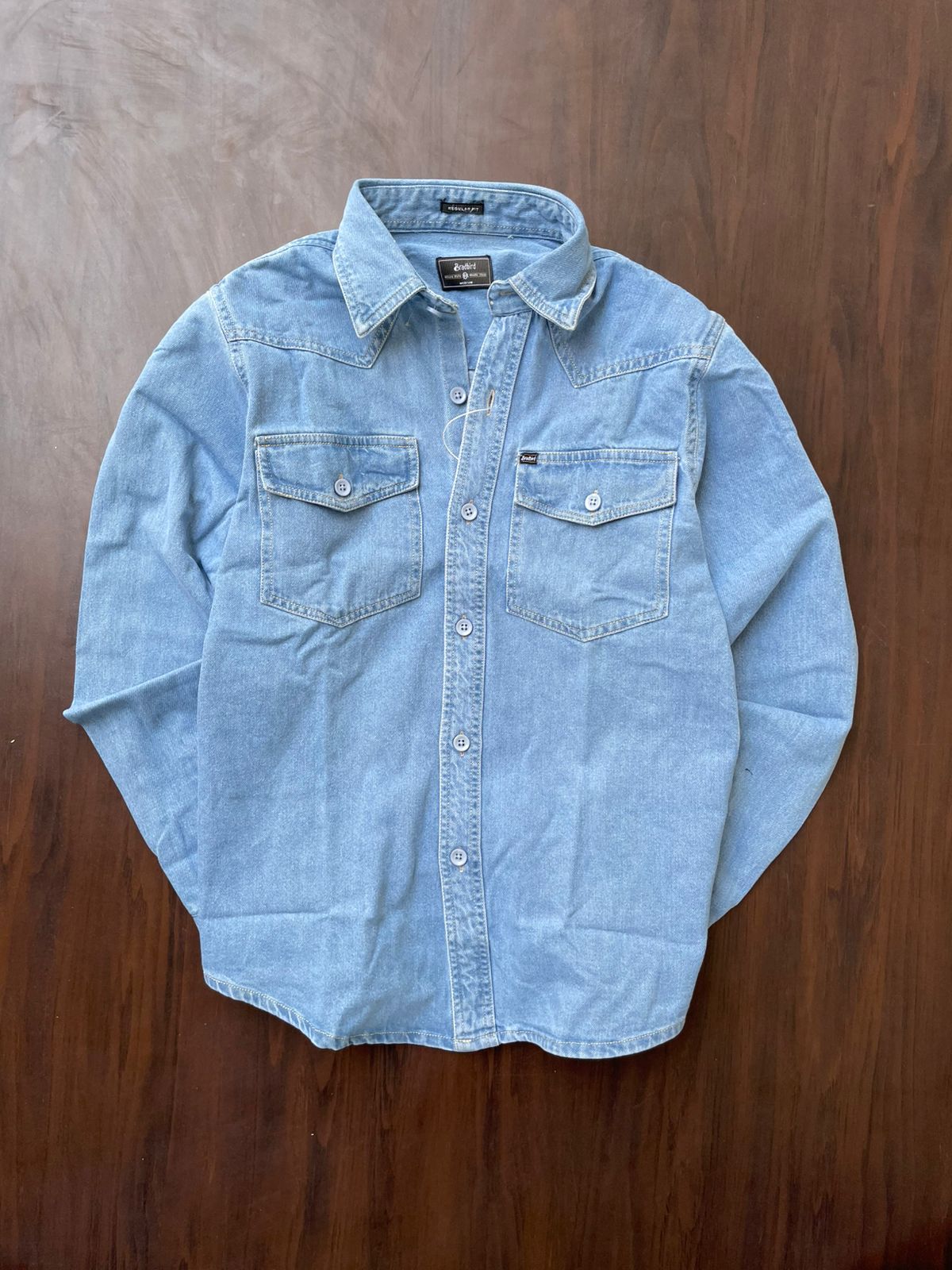 Light blue denim shirt laid flat, button front and two chest pockets