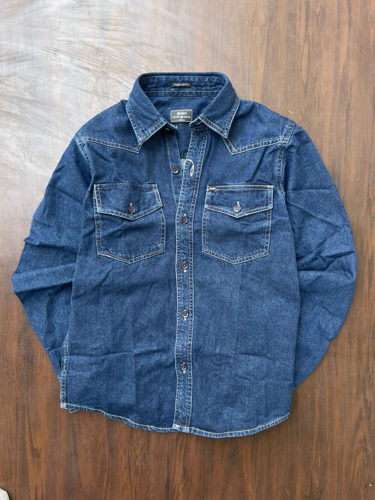 Blue denim western-style shirt laid flat, button front and flap chest pockets
