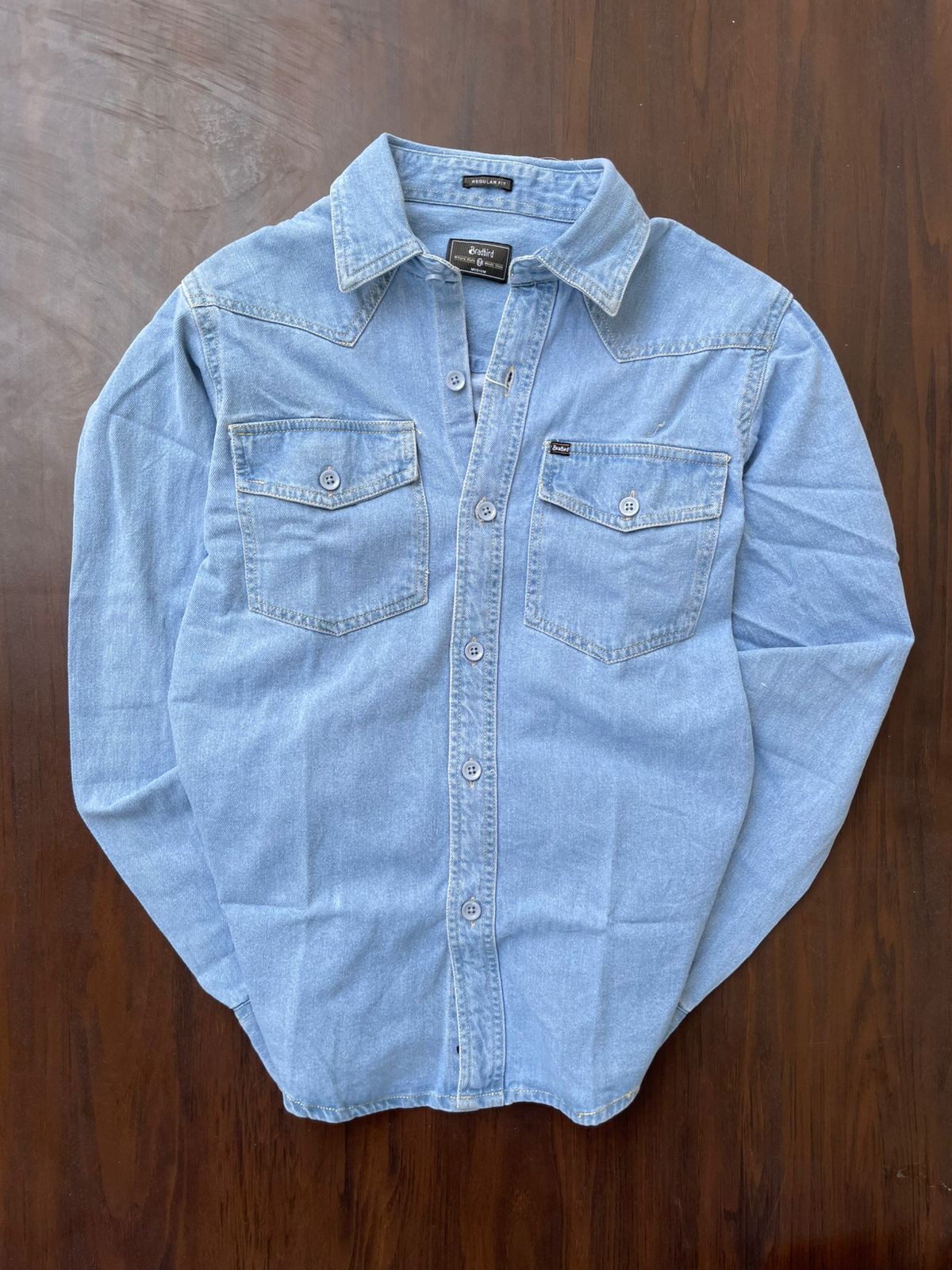 Light wash denim over-shirt laid flat, snap-button placket and chest pockets