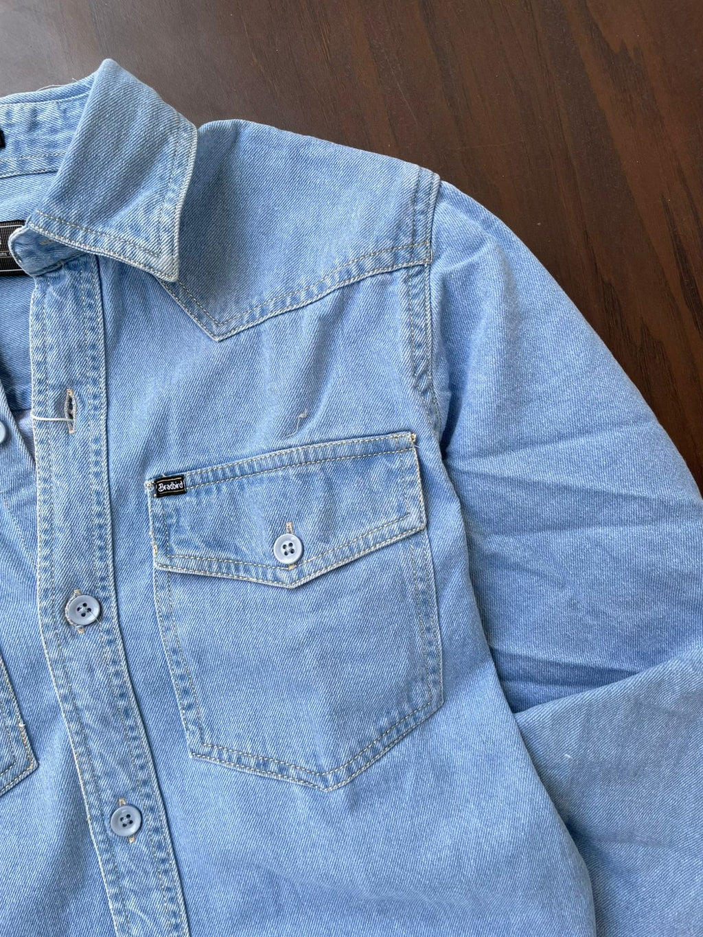 Light wash denim over-shirt close-up: flap chest pocket and snap buttons