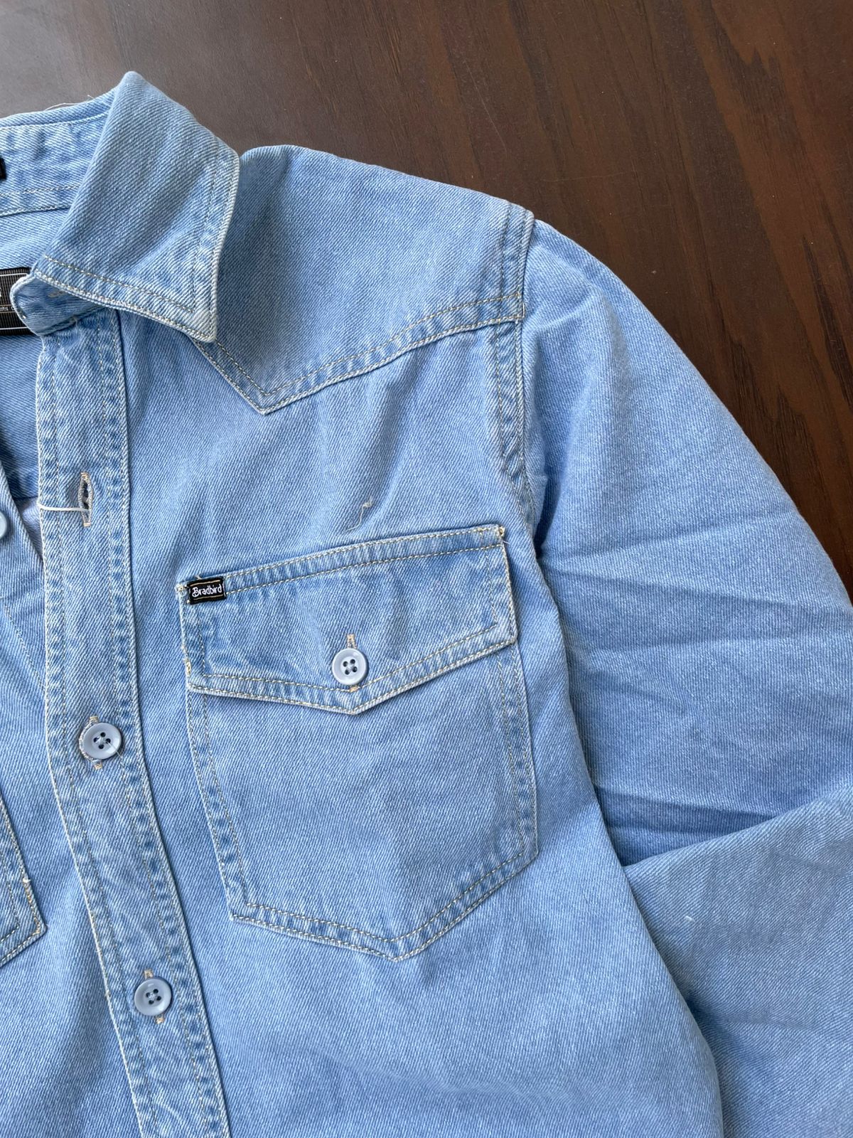 Light wash denim over-shirt close-up: flap chest pocket and snap buttons