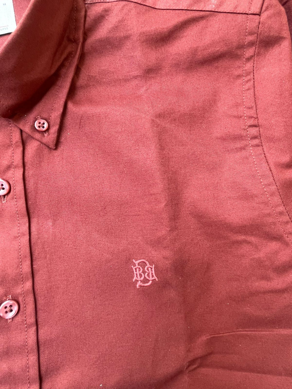Maroon textured oxford shirt close-up, tonal monogram at chest and button placket