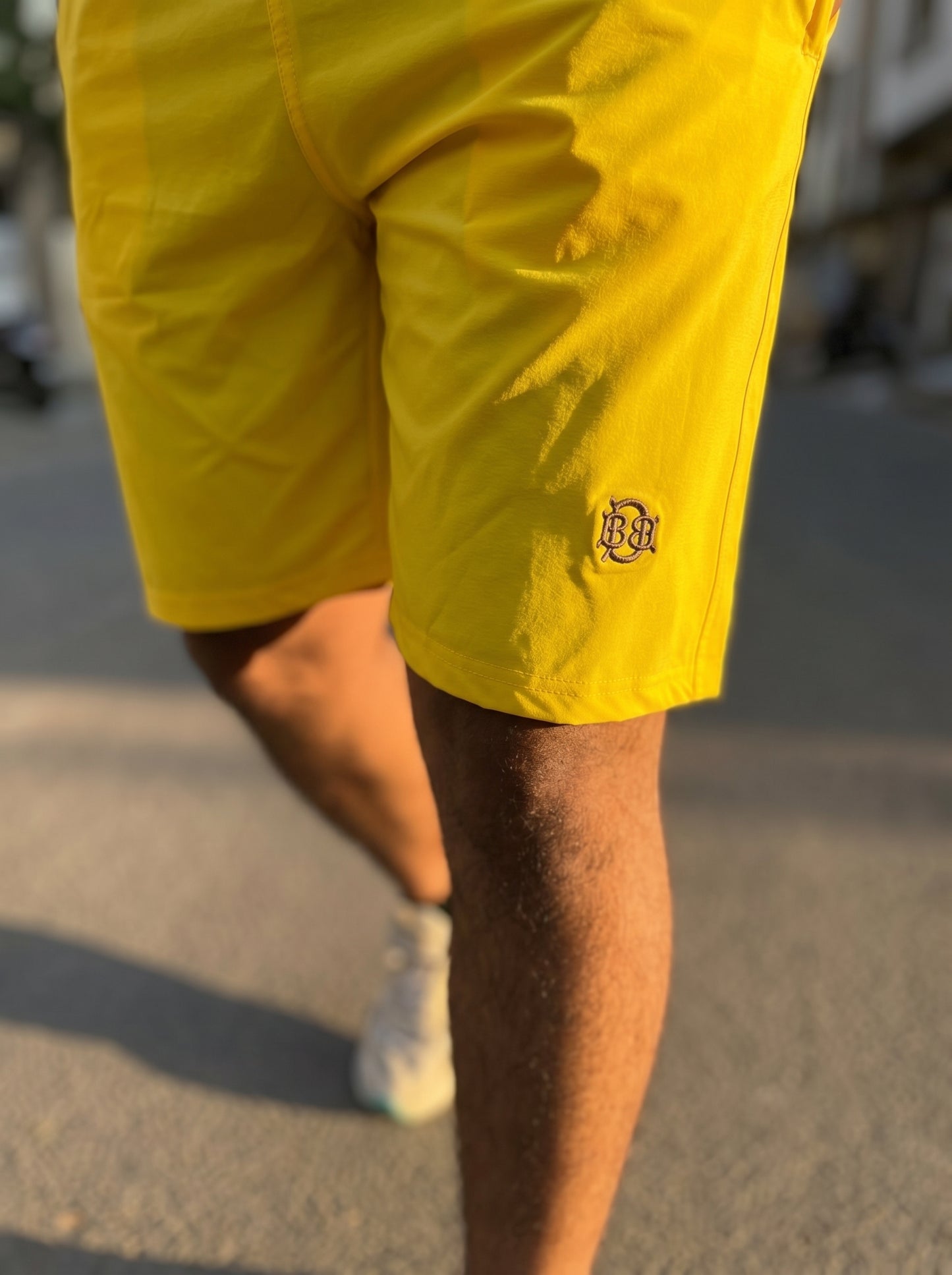 Bright yellow shorts close-up: small BQ logo on leg, smooth lightweight fabric
